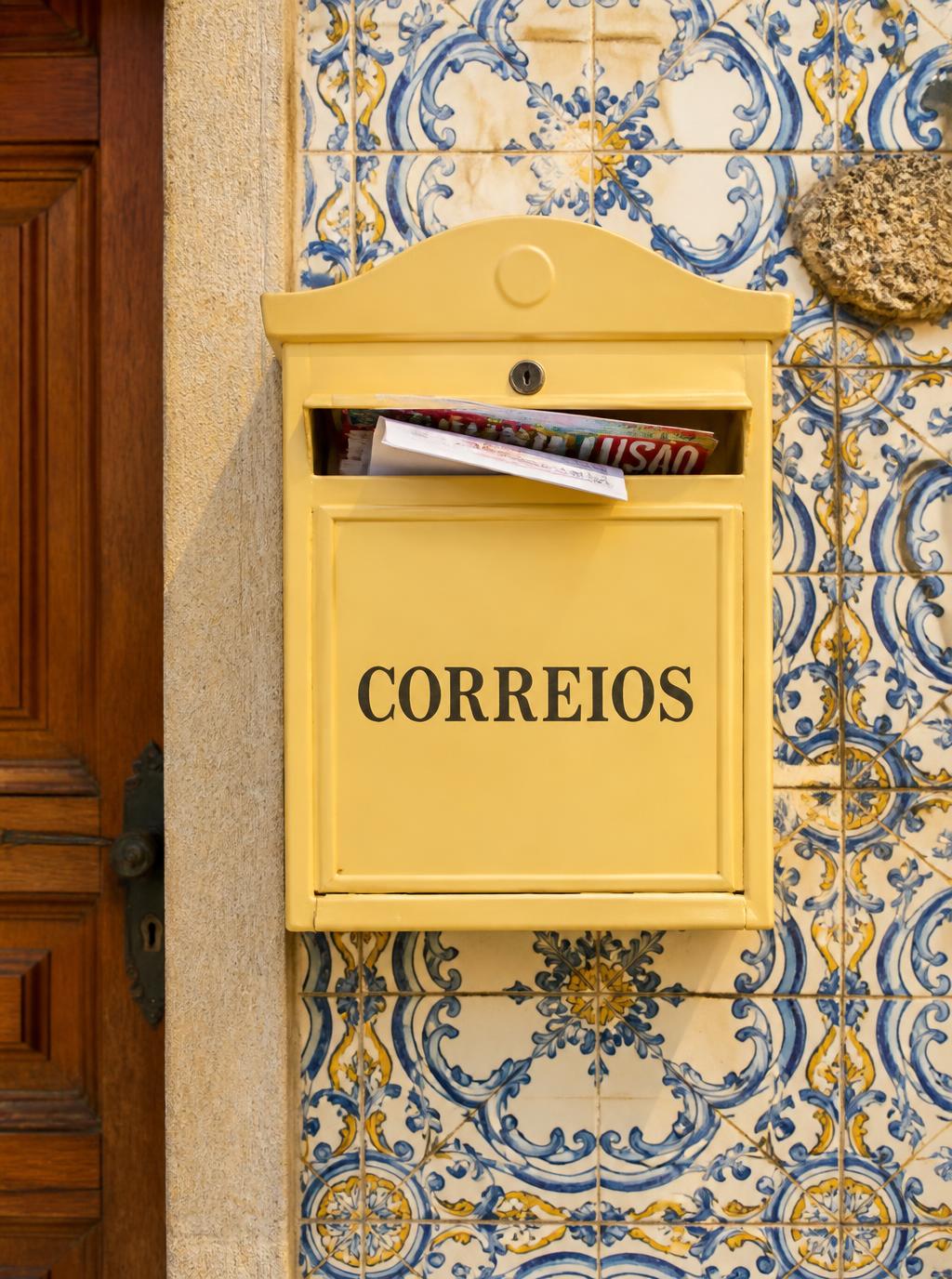 Private residential mailbox with a few letters and a magazine, mounted on a traditional Porto azulejo-tiled wall next to a wooden door